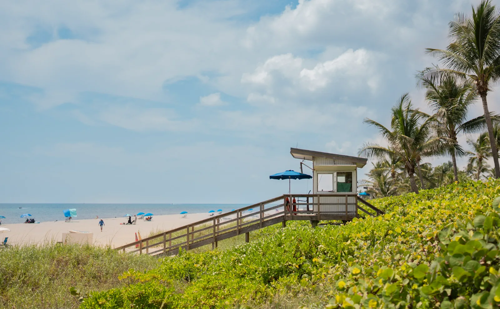 Lifeguard tower, palms and blue umbrellas at Oceanfront Park Beach in Boynton Beach, Florida