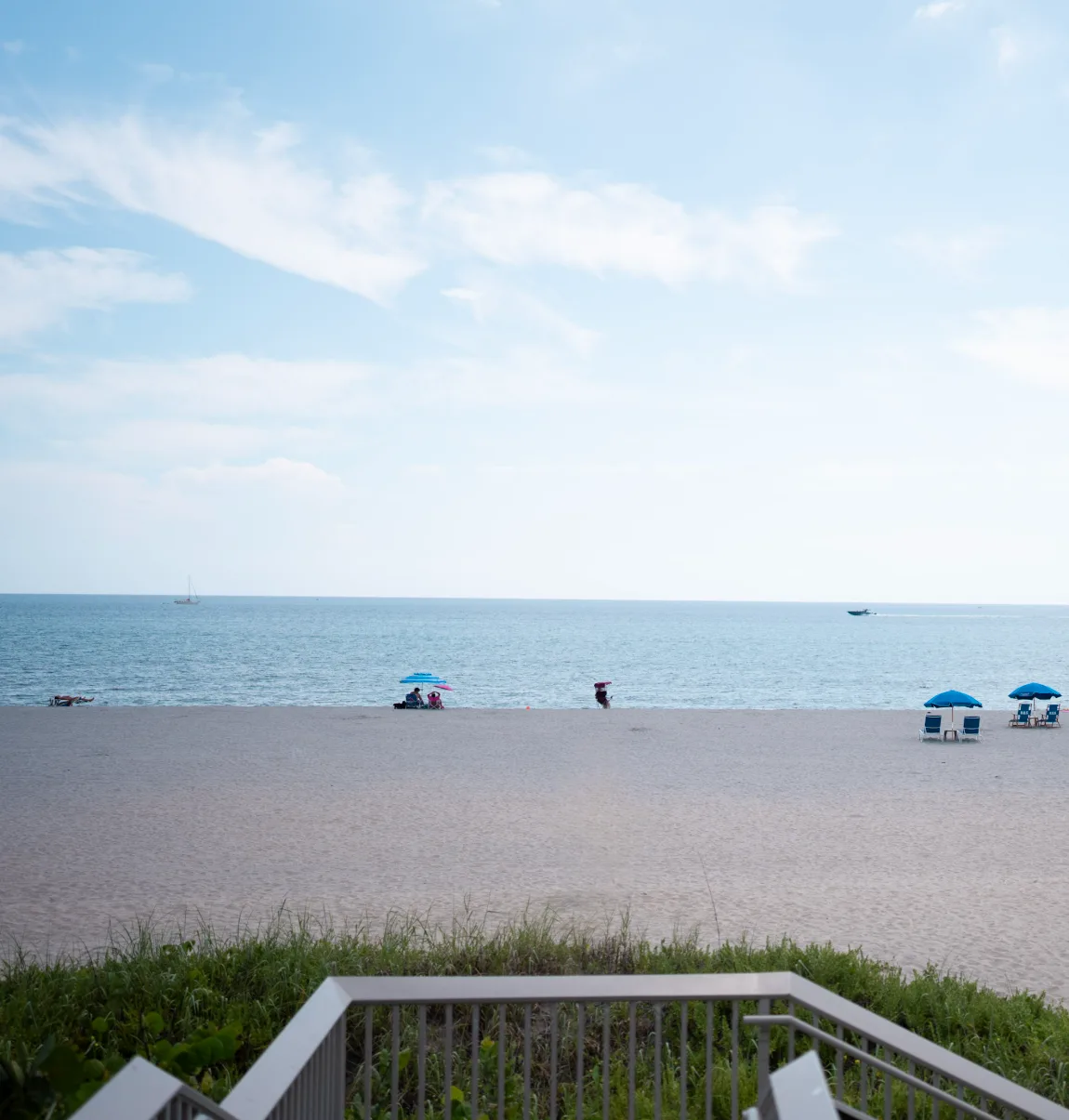 Calm blue ocean, boats and beach umbrellas seen from the boardwalk at Oceanfront Park, Boynton Beach