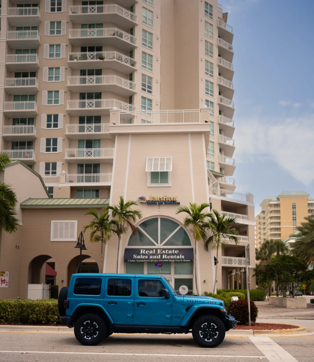 Beachside condo tower at Casa Costa in Boynton Beach with palms and a blue Jeep parked out front