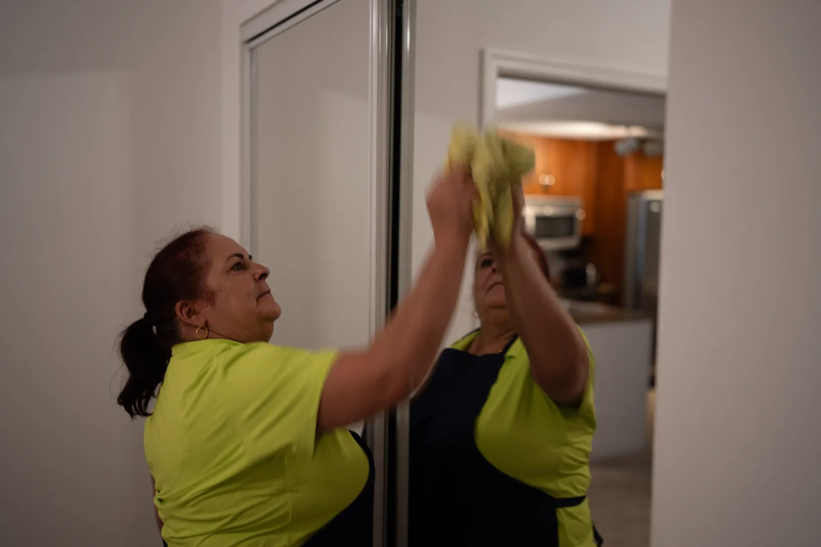 Tidy Mom cleaner in a lime shirt wiping a mirrored closet door during an Airbnb turnover in Boynton Beach